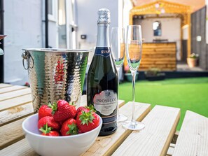 A bottle of prosecco, two glasses, and a bowl of strawberries on a wooden table.