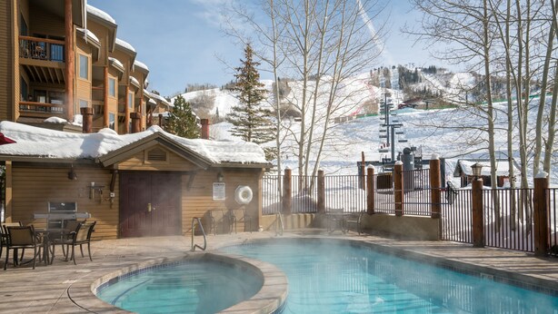 A pool area with a hot tub, outdoor seating, and a view of a snowy mountain.