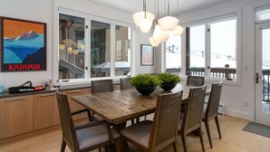 A modern dining area with a wooden table and chairs, a large window with a view, and a framed picture on the wall.