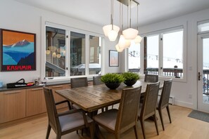 Enjoy meals in this dining area with a wooden table and six chairs, illuminated by pendant lights and offering a view of the outside through large windows.