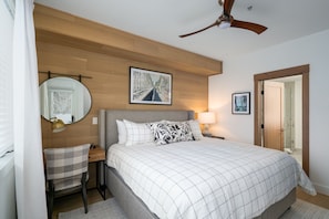 Une chambre à coucher comprenant un lit, un bureau, une chaise, un ventilateur de plafond et un tableau encadré accroché au mur.