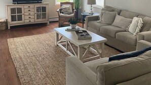 Een woonkamer met een televisie, een bank, een salontafel en een schilderij aan de muur.