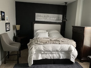 Un dormitorio con cama, una silla, cómoda y lámpara de pared.