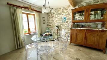 Un coin repas avec une table et des chaises en verre, un mur en pierre, des meubles en bois et une fenêtre avec des rideaux.