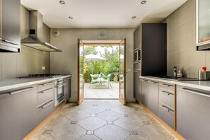 A modern kitchen with stainless steel appliances, a hexagonal tile floor, and a view of a patio with outdoor furniture. - Gîte-Deluxe-Countryside view-Ensuite (Servies-en-Val)
