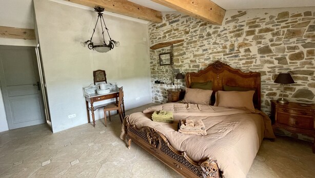 Une chambre avec un mur en pierre, un cadre de lit en bois, un bureau avec une chaise et une table de chevet avec une lampe.