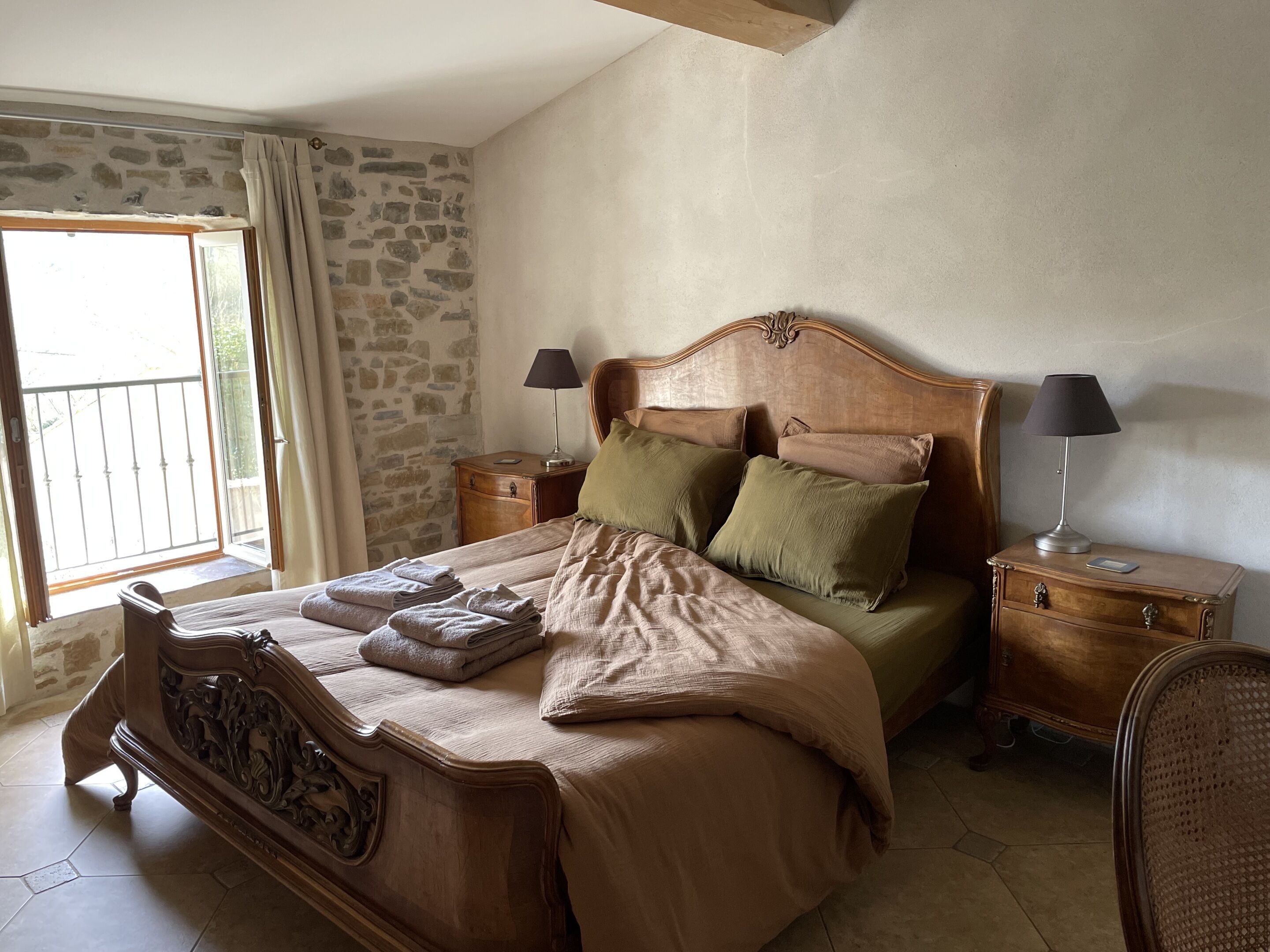 Een slaapkamer met een groot bed, twee nachtkastjes, een raam met gordijnen en een stenen muur.