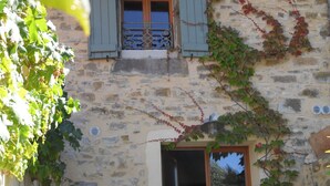 Un bâtiment en pierre avec une fenêtre et des volets, une porte et une table entourée de chaises.
