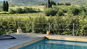 Une piscine avec une terrasse en bois et une vue sur un vignoble et des collines en arrière-plan.