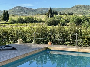 A swimming pool with a wooden deck and a view of a vineyard and hills in the background.