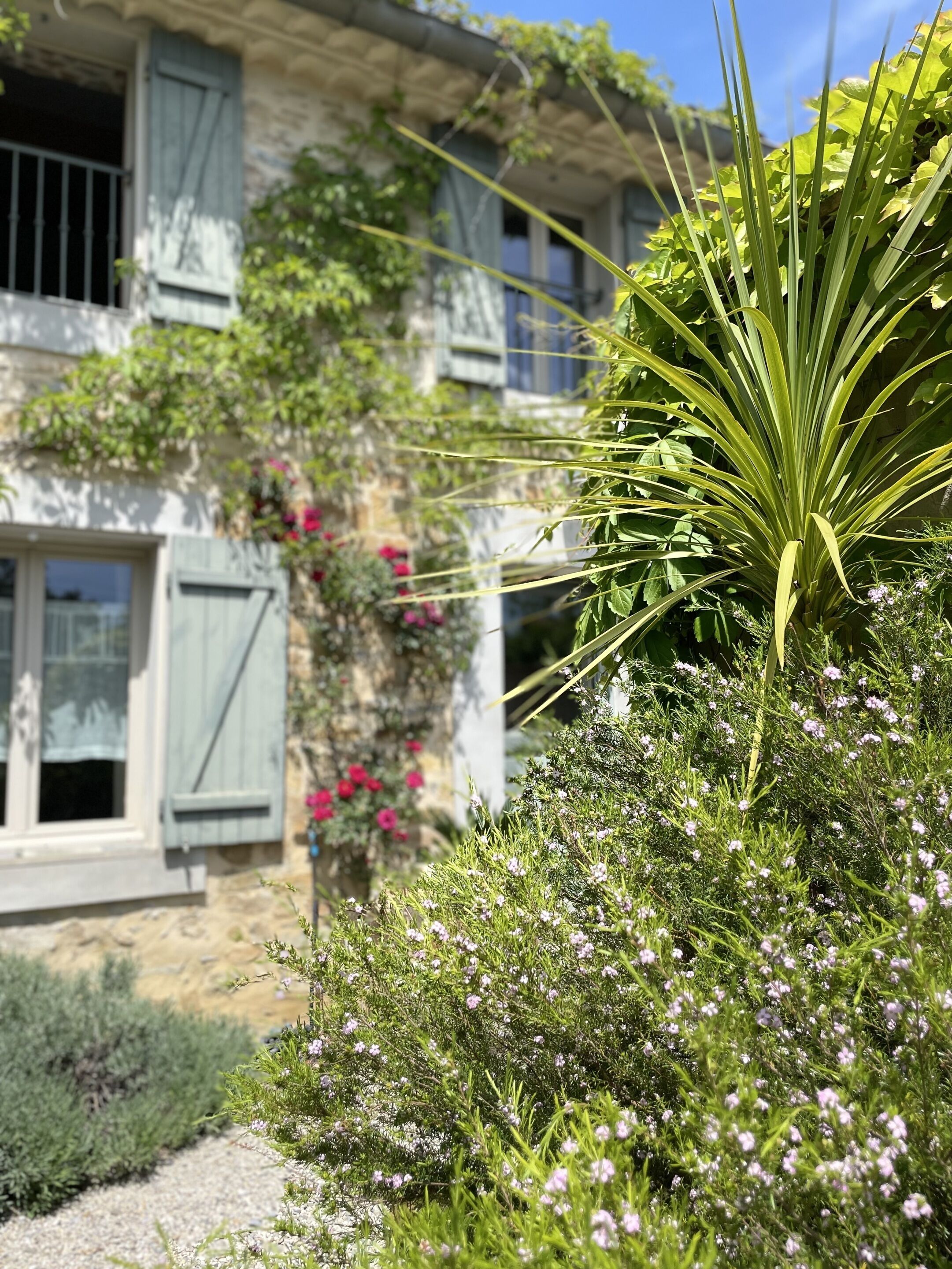 A stone building with a garden in front, featuring a variety of plants and flowers.