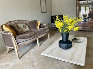 A living room with a brown sofa, a black vase with yellow flowers, and a tiled floor.