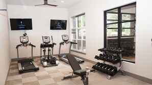 Ein Fitnessraum mit Laufbändern, Crosstrainern, einer Bank und einem Hantelgestell.