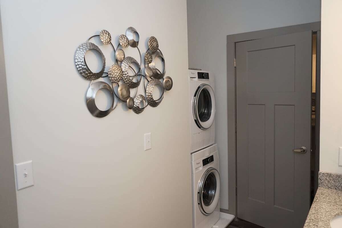 A laundry room with a wall-mounted metal sculpture, a stacked washer and dryer, and a closed door.