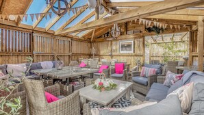 A covered outdoor seating area with wicker furniture, a glass-top table, and a chandelier. - 8 bedroom accommodation in Horsemans Green (Horsemans Green)