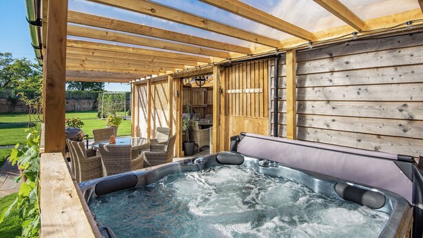 A hot tub under a wooden pergola with a view of a garden and a fence. - 8 bedroom accommodation in Horsemans Green (Horsemans Green)