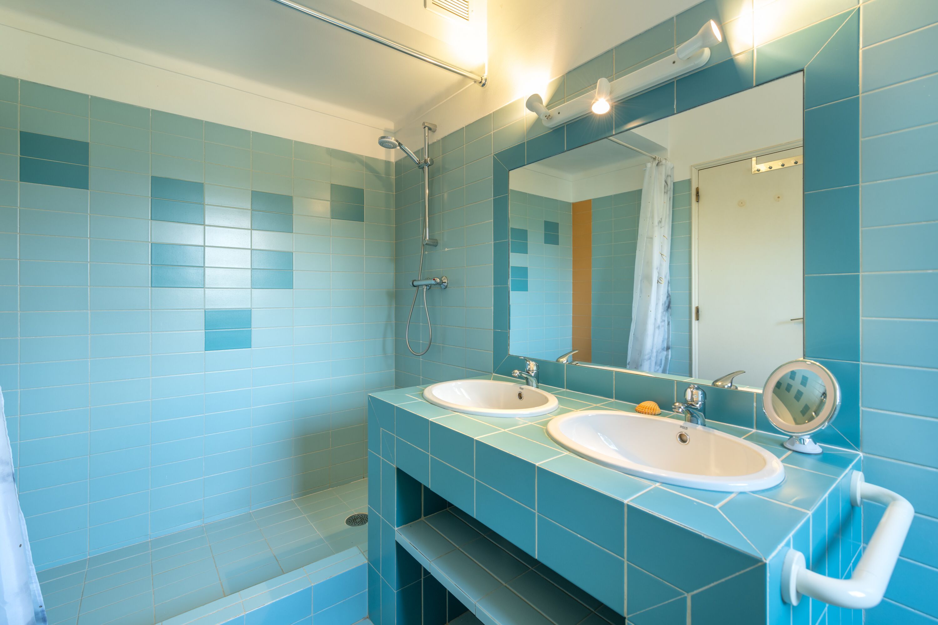 Een badkamer met twee wasbakken, een douche en een spiegel.
