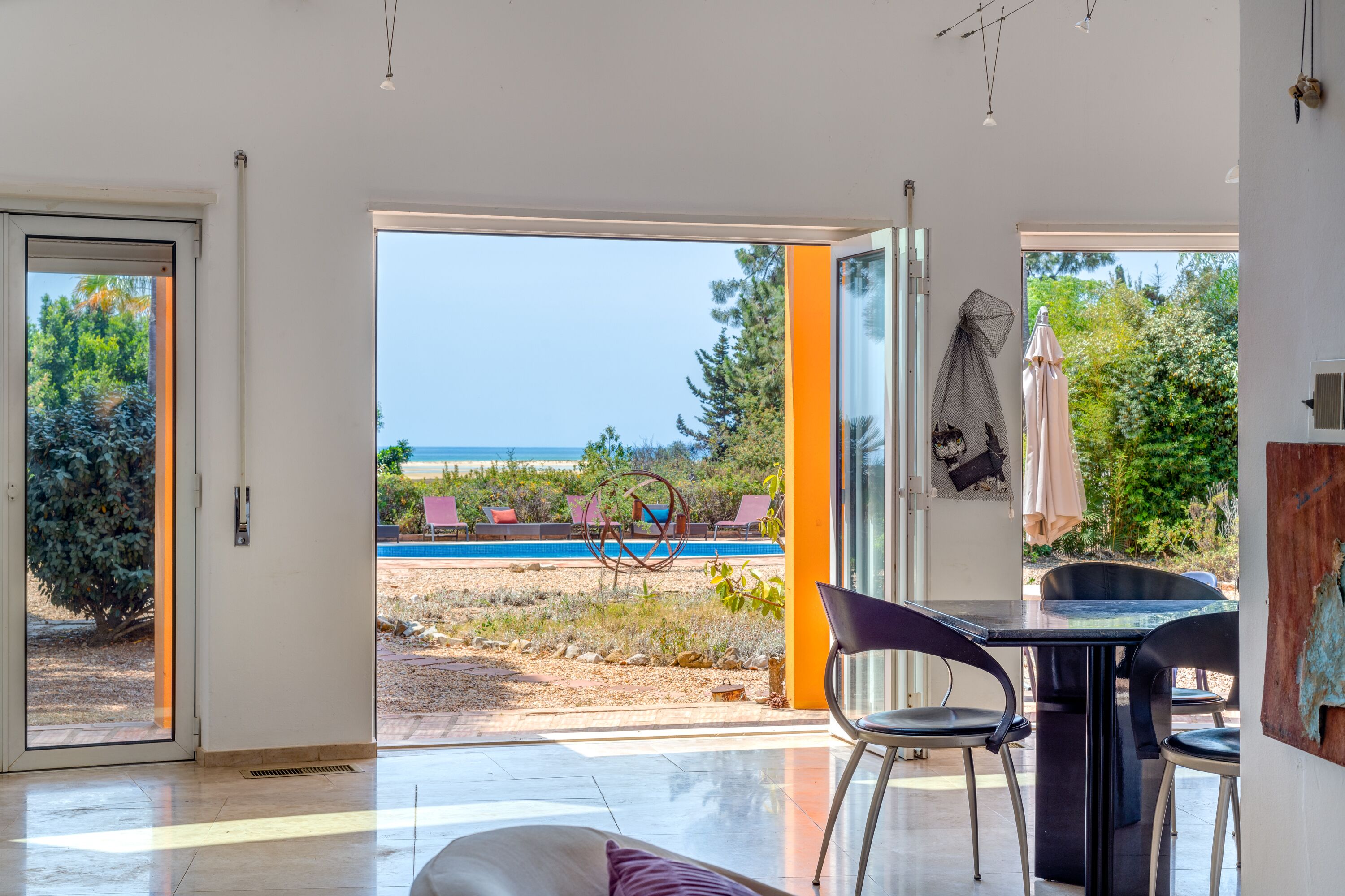 A modern room with a glass door leading to a pool area, a dining table with chairs, and a view of the sea.