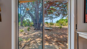 Une porte-fenêtre coulissante donne sur un patio extérieur agrémenté d’un chemin de pierre, d’un banc en bois et d’une vue sur l’océan.