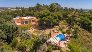 Une grande maison à deux étages, dotée d’une piscine et d’un espace extérieur aménagé, le tout entouré d’une végétation luxuriante.