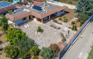 A residential building with a tiled roof, solar panels, a patio with outdoor furniture, and a garden area.