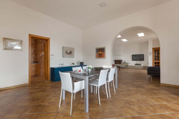 Un salón amplio con una mesa de comedor y sillas, una cocina al fondo y un televisor montado en la pared.