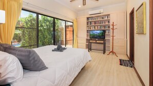 Une chambre avec un grand lit, une télévision, une bibliothèque et une vue sur la verdure environnante.