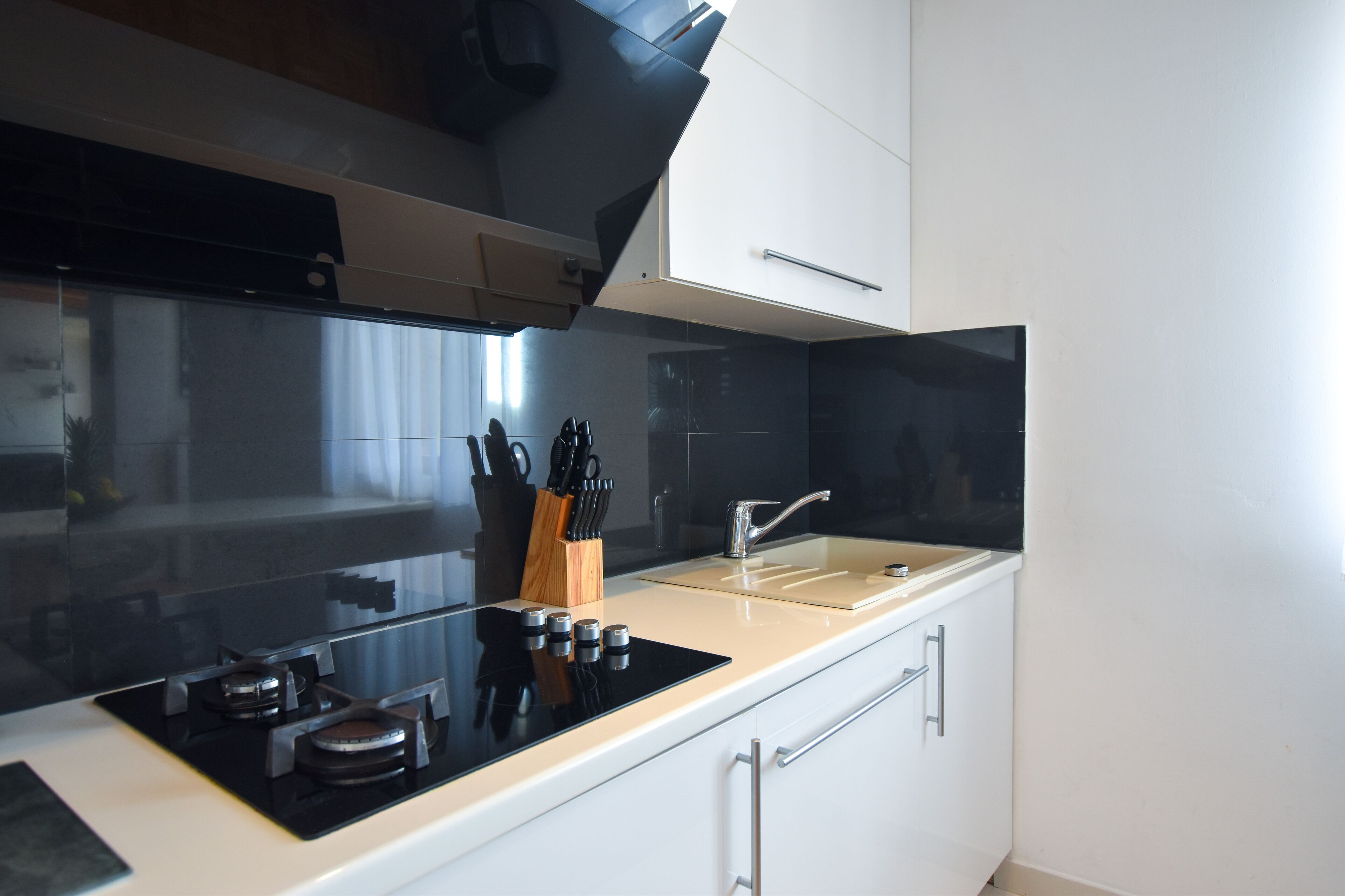 A modern kitchen with a black stovetop, white cabinets, and a stainless steel sink.