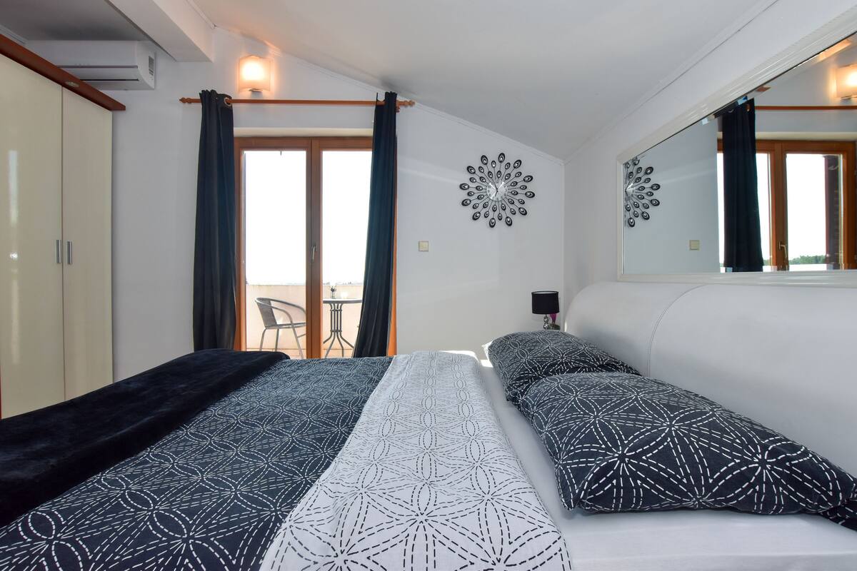A bedroom with a bed, a wardrobe, a mirror, and a view of the outdoors.