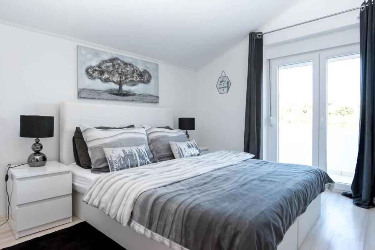 A bedroom with a bed, nightstands, a lamp, a painting, and a window with curtains.