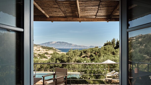 A balcony with a wooden ceiling, a pool, and a view of a mountainous landscape. - Strofilia Stone Residences (Zakynthos)