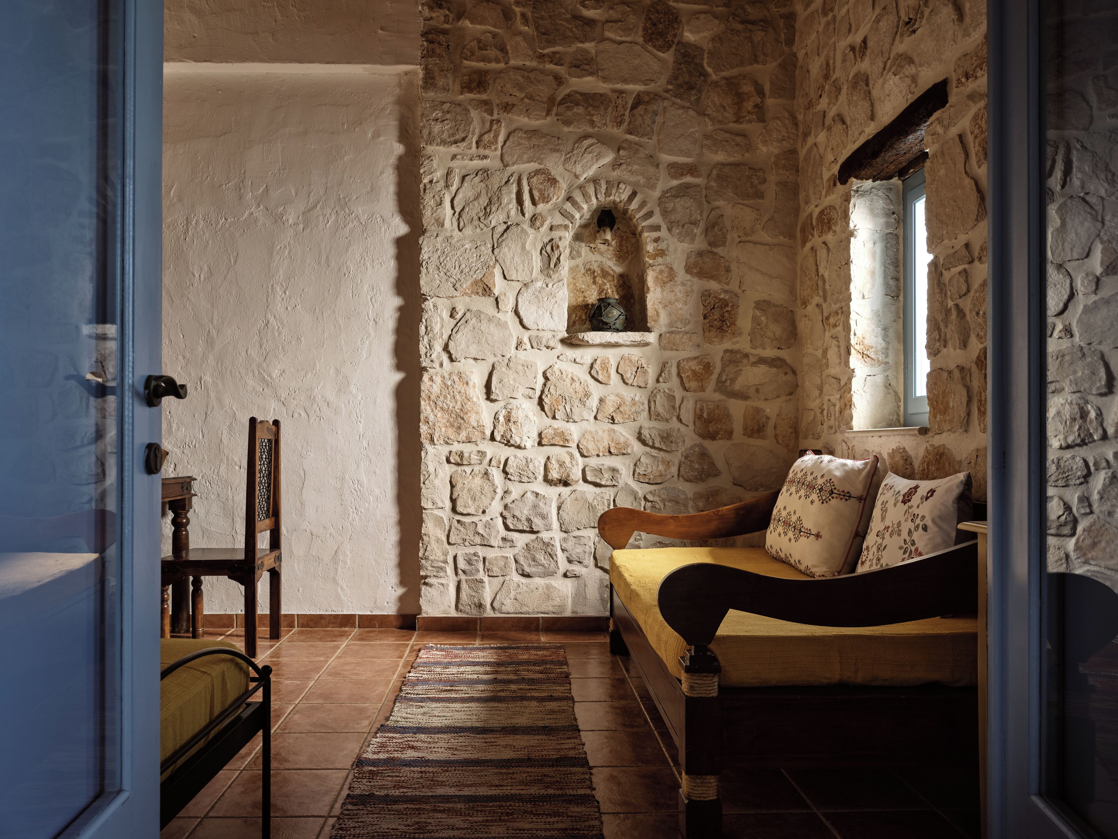 A cozy room with a stone wall, a wooden bench, a small window, and a door.