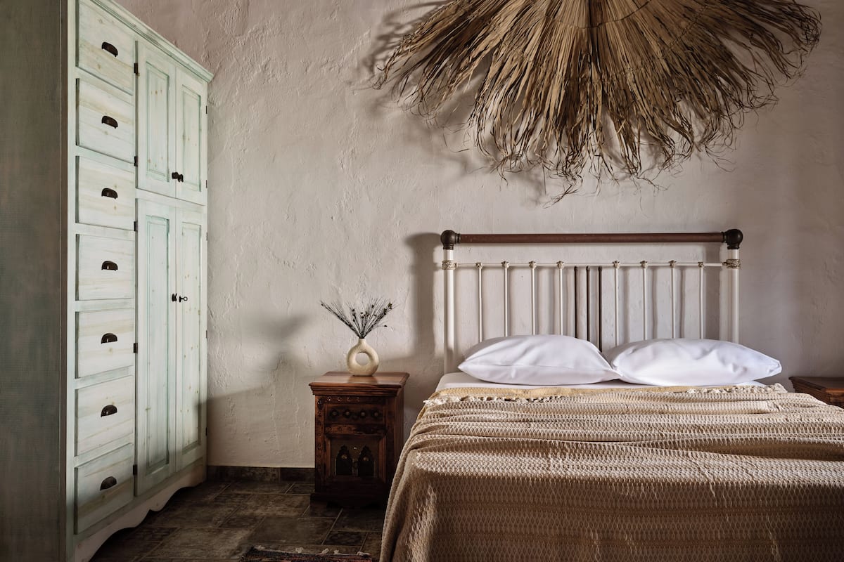 A bedroom with a bed, a nightstand, a dresser, and a hanging plant.