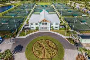 Vue aérienne d’un complexe sportif comprenant plusieurs courts de tennis, un bâtiment central doté d’un toit végétalisé et un espace paysager circulaire.