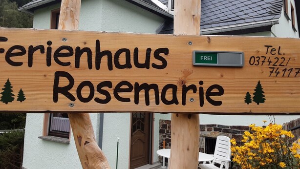 Un letrero de madera con el nombre 'Ferienhaus Rosemary' y un número de teléfono.