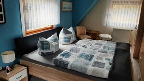 Un dormitorio con cama, almohadas, una mesita de noche, una silla y una ventana.