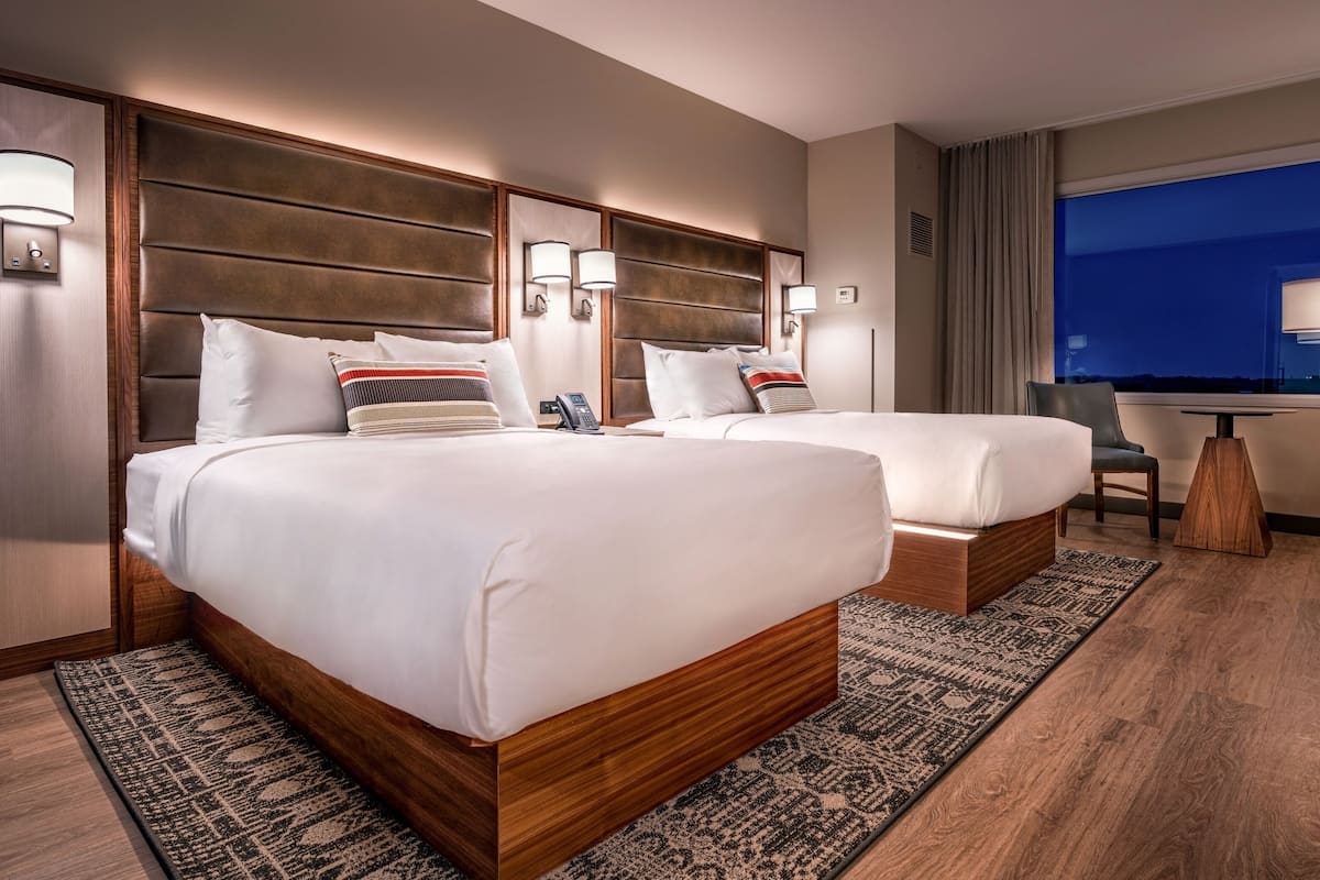 Una habitación de hotel con dos camas, un escritorio y un ventanal grande.