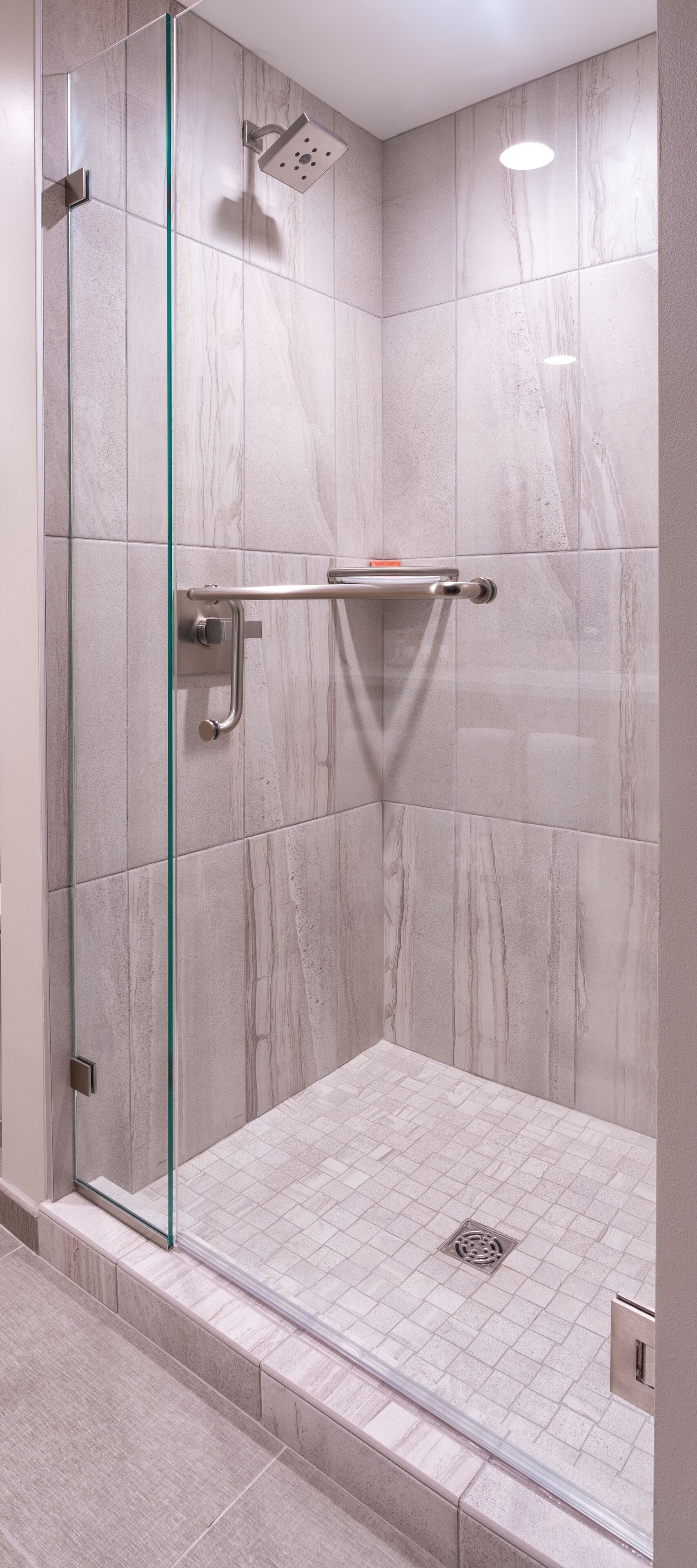 A modern shower with glass doors, a handheld showerhead, and a glass shelf.