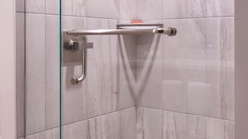 A modern shower with glass doors, a handheld showerhead, and a glass shelf.