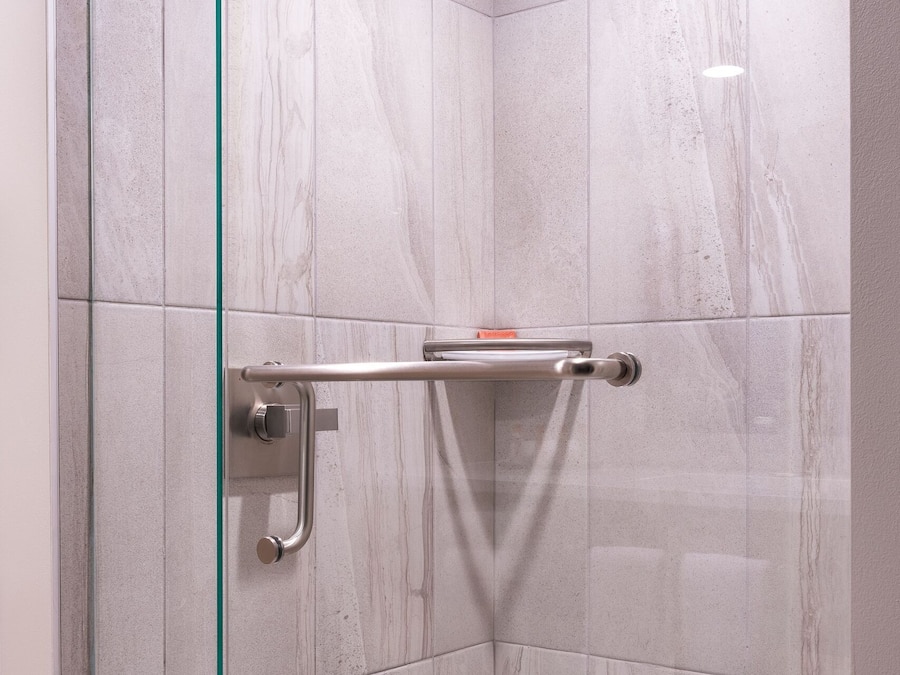 A modern shower with glass doors, a handheld showerhead, and a glass shelf.