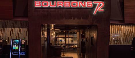 The entrance to a hotel named "BOURBONST72" with a modern design, featuring a digital signboard and a reception area visible through the glass doors.