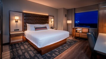 Una habitación de hotel moderna con una cama grande, mesitas de noche, un escritorio y vistas al cielo nocturno.