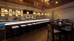Een bar met een lange toonbank, verschillende krukken en hangende pendelverlichting.