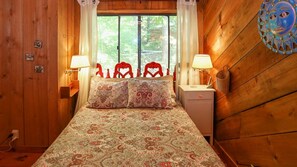 Una habitación de madera con una cama, dos mesitas de noche y una ventana con cortinas.