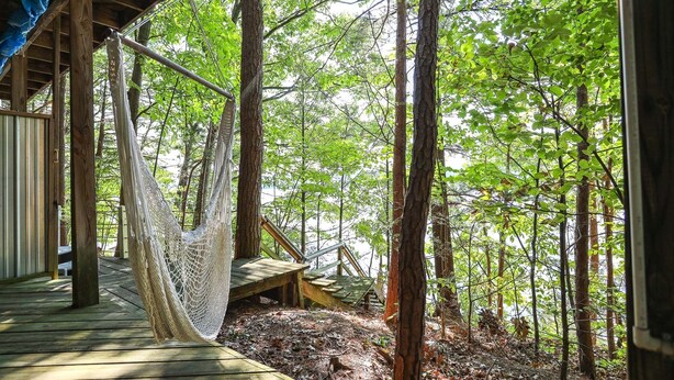 A hammock hanging from a wooden structure in a forested area with a wooden deck and a small wooden platform.