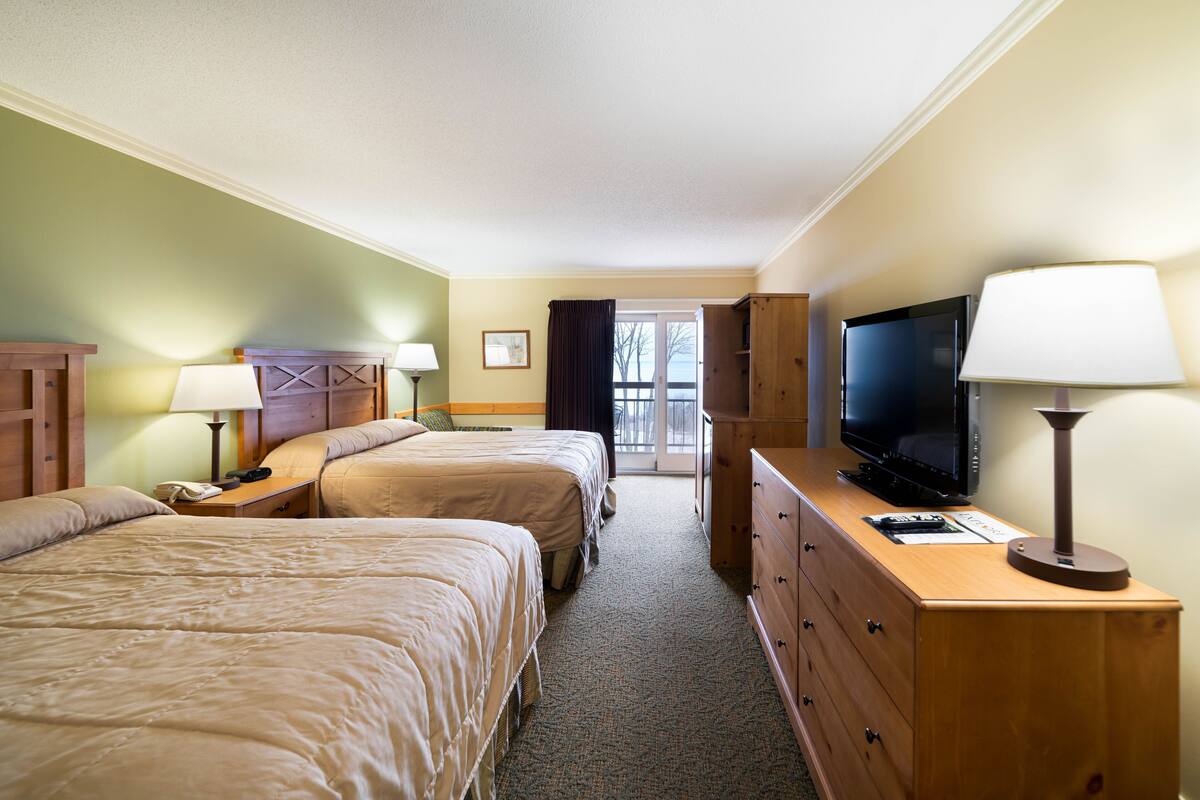 Habitación de hotel con dos camas, televisor, cómoda y ventana con cortinas.