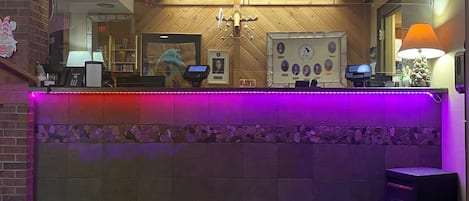 A reception area with a wooden counter, a 'Welcome Friends' sign, and a small birdhouse decoration.