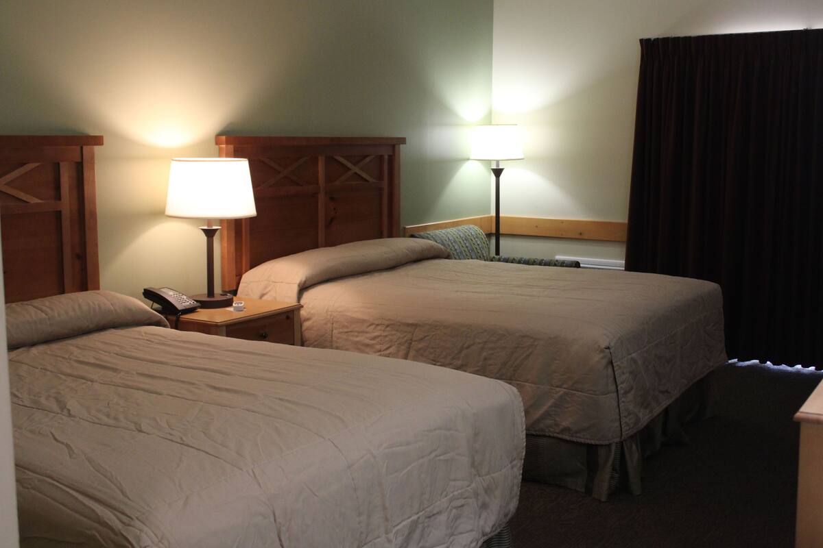 Habitación de hotel con dos camas, una mesita de noche con lámpara, teléfono y cortina.