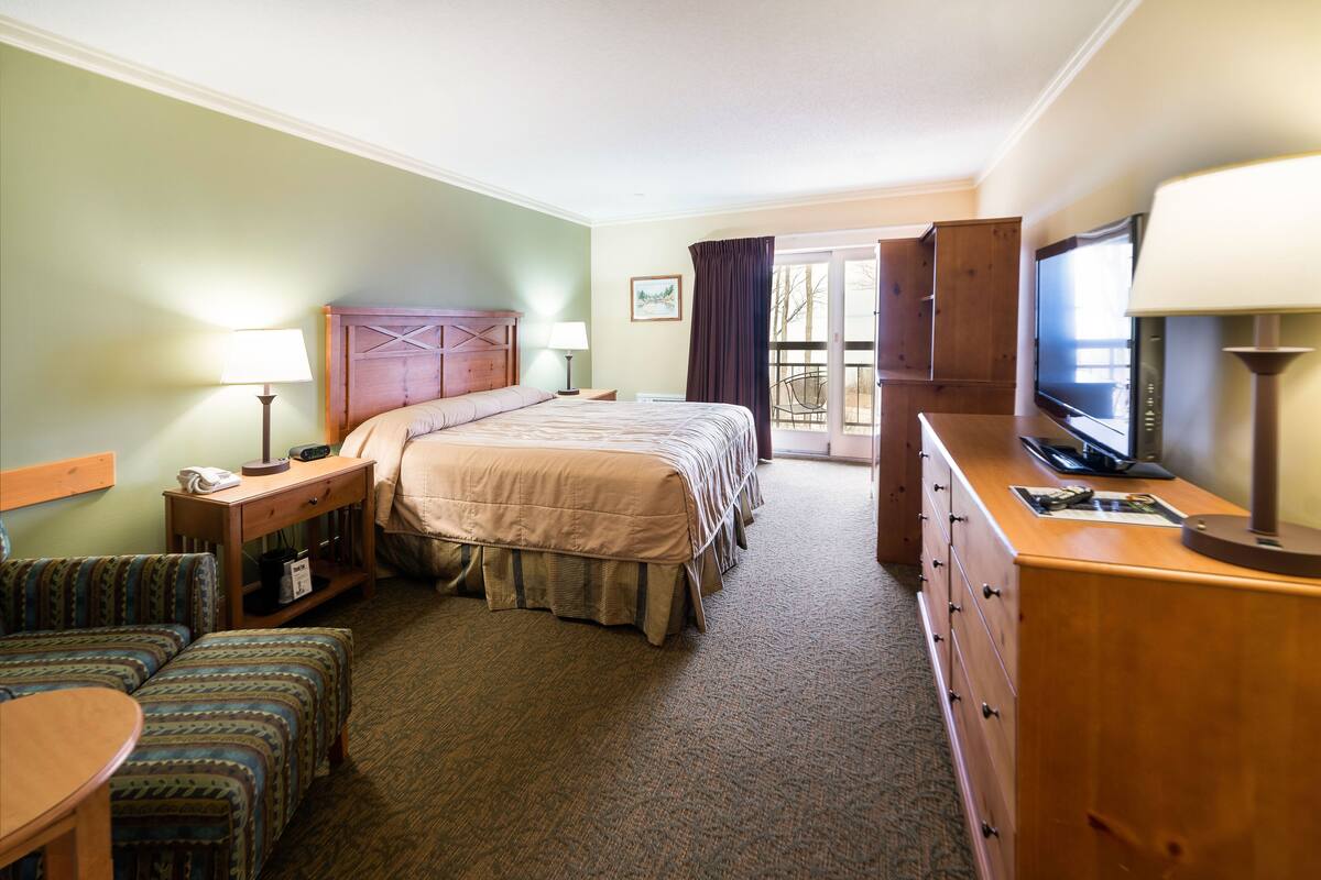Habitación de hotel con cama, televisión, escritorio con lámpara, sillón y sofá.
