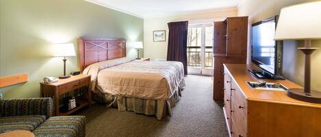 A hotel room with a bed, a television, a desk with a lamp, a chair, and a sofa.
